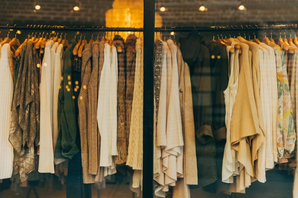A rail of coats and knits in cream, camel and olive seen through a shop window