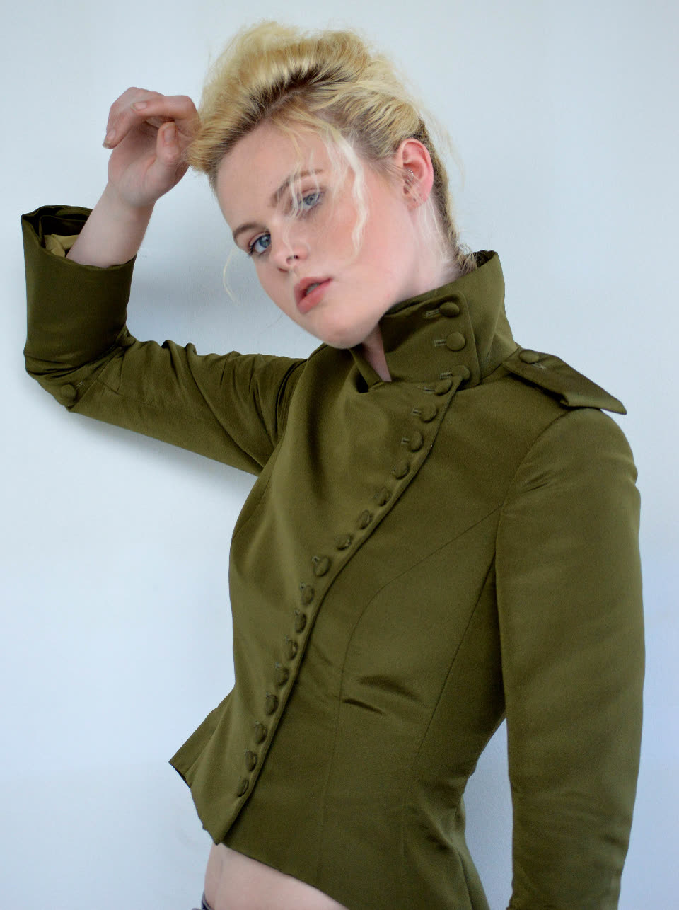 Model in a buttoned, high-collared olive jacket, one hand raised to her hair